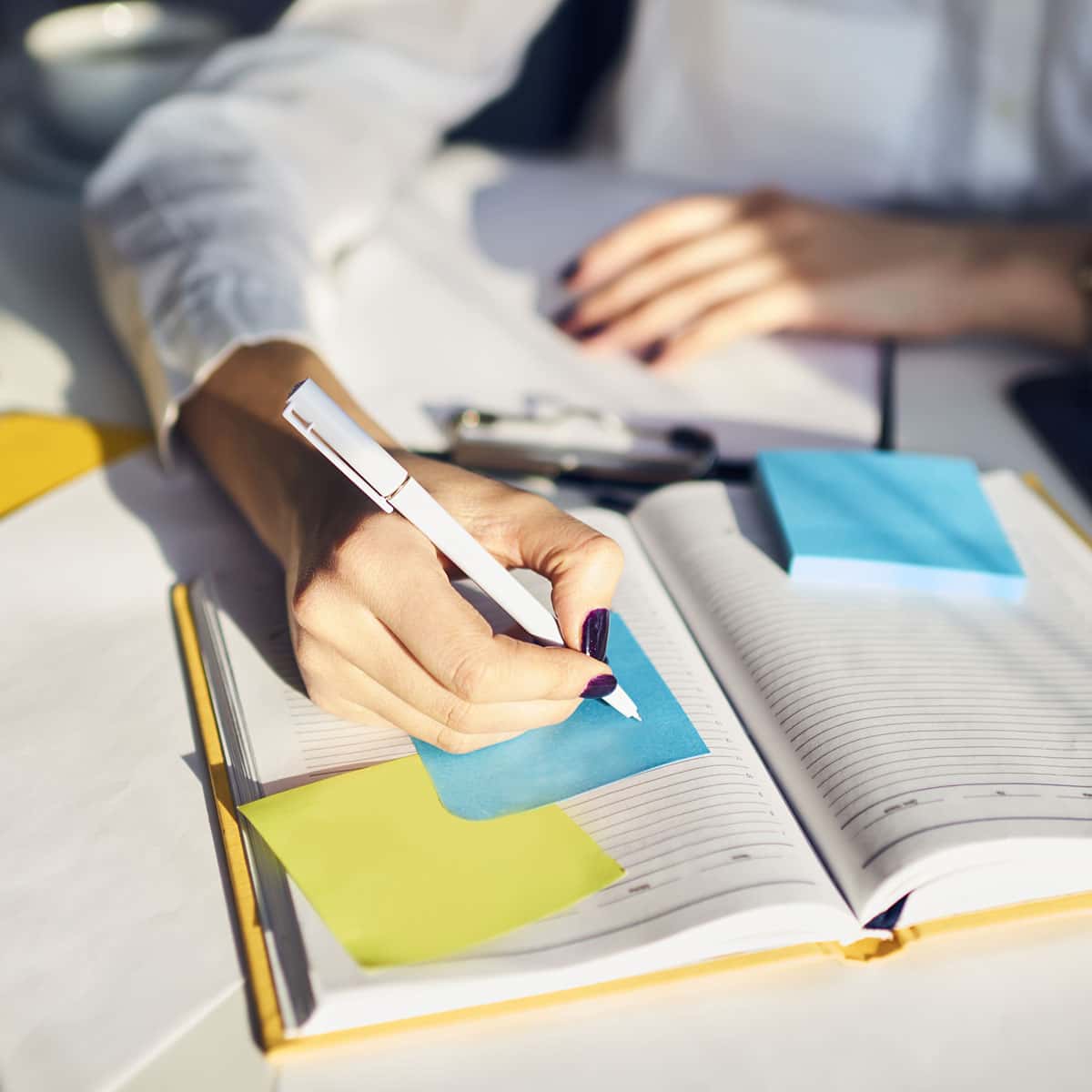person working at desk writing on a post it on a book