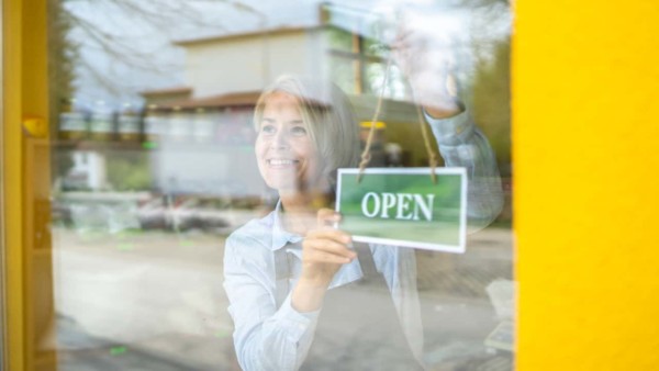 Image of someone hanging an 'open' sign on their door.