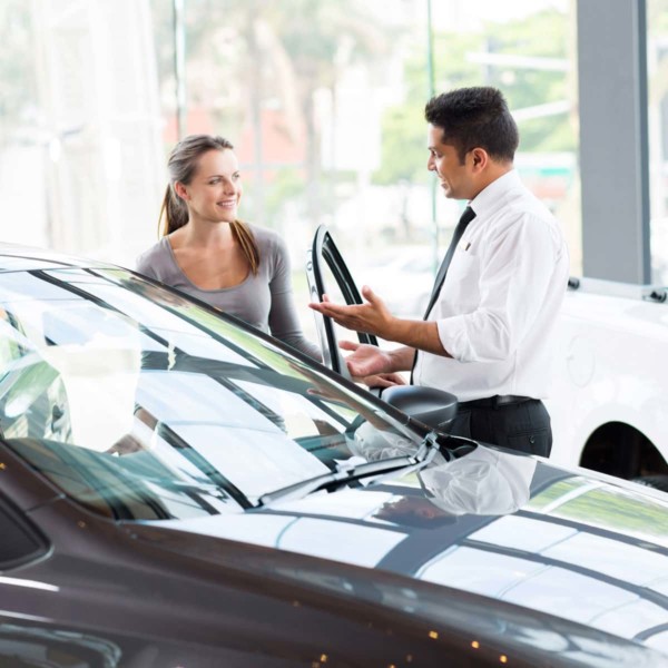 Image of a sales person with a customer looking at a car in a dealership.
