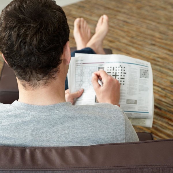 man doing sudoku on his couch in the newspaper
