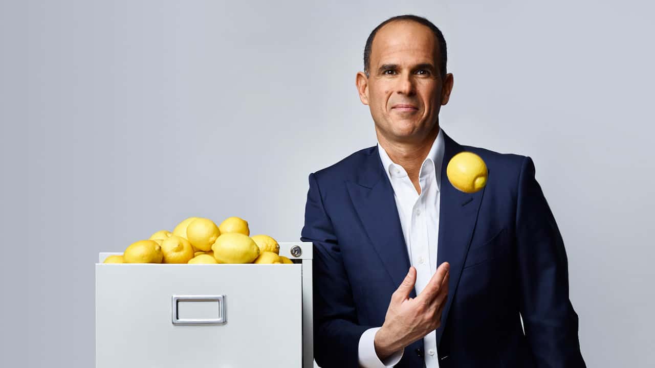 Image of Marcus Lemonis standing next to a file cabinet filled with lemons.
