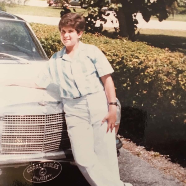 Image of Marcus Lemonis as a kid leaning on a car.