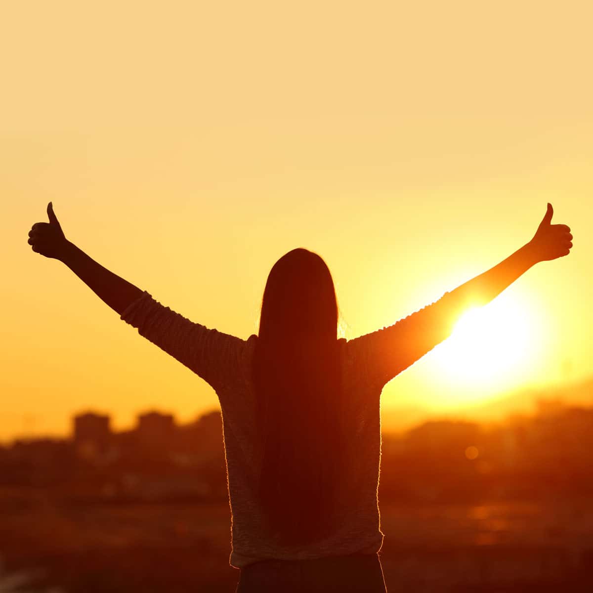 person standing in front of a sunset with her thumbs up
