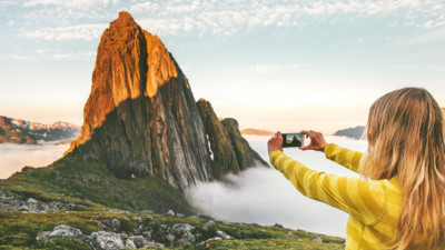 women photographing a mountain surrounded by fog in a yellow shirt