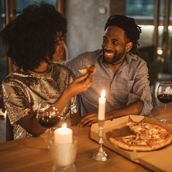 Image of a couple having a dinner date with pizza and wine by candlelight.